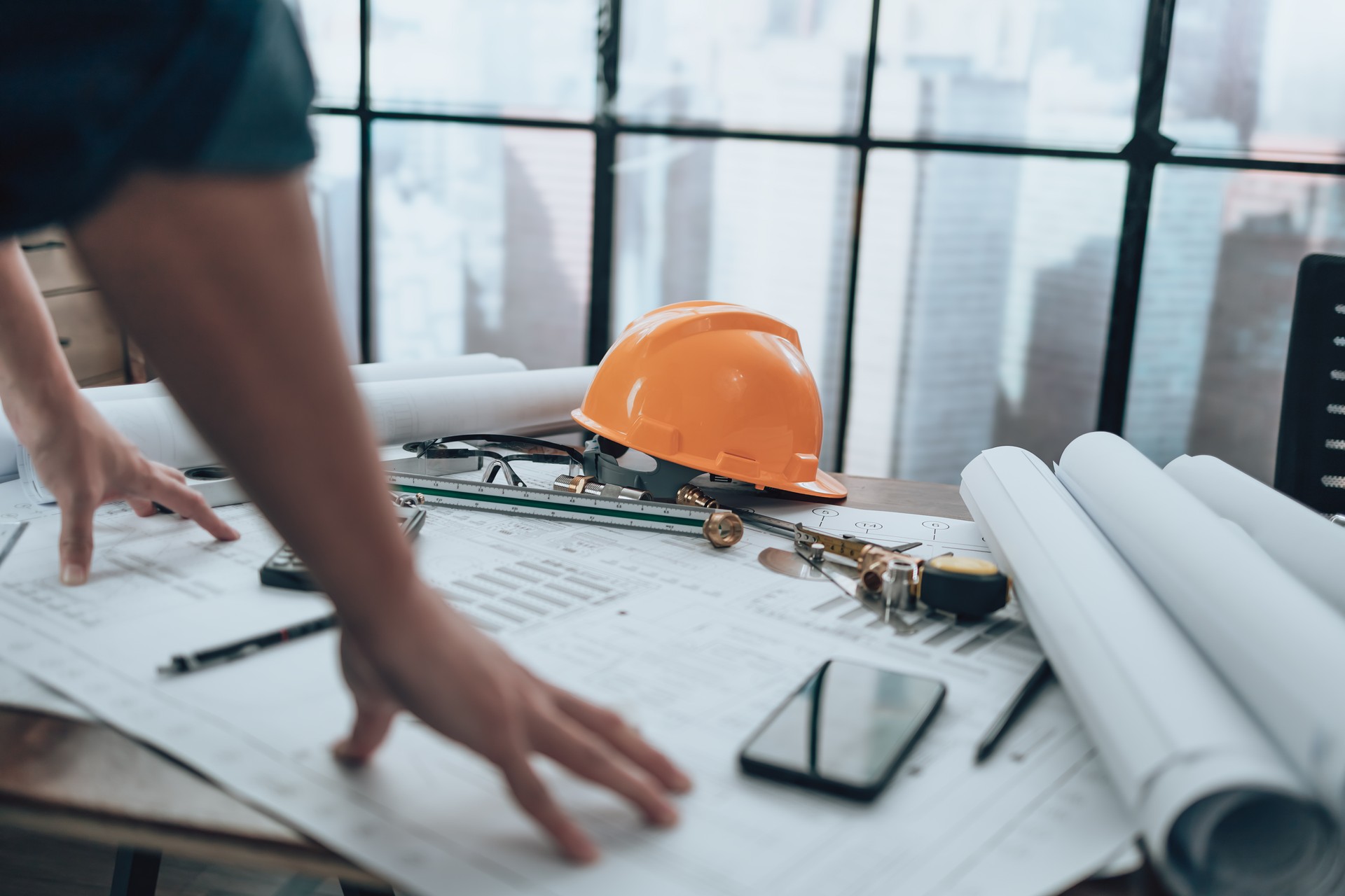 Engineer safety helmet with drawings inspection on the office desk and Calculator, triangle ruler, safety glasses, compass, vernier caliper on Blueprint. Engineer, Architect, Industry and factory concept.